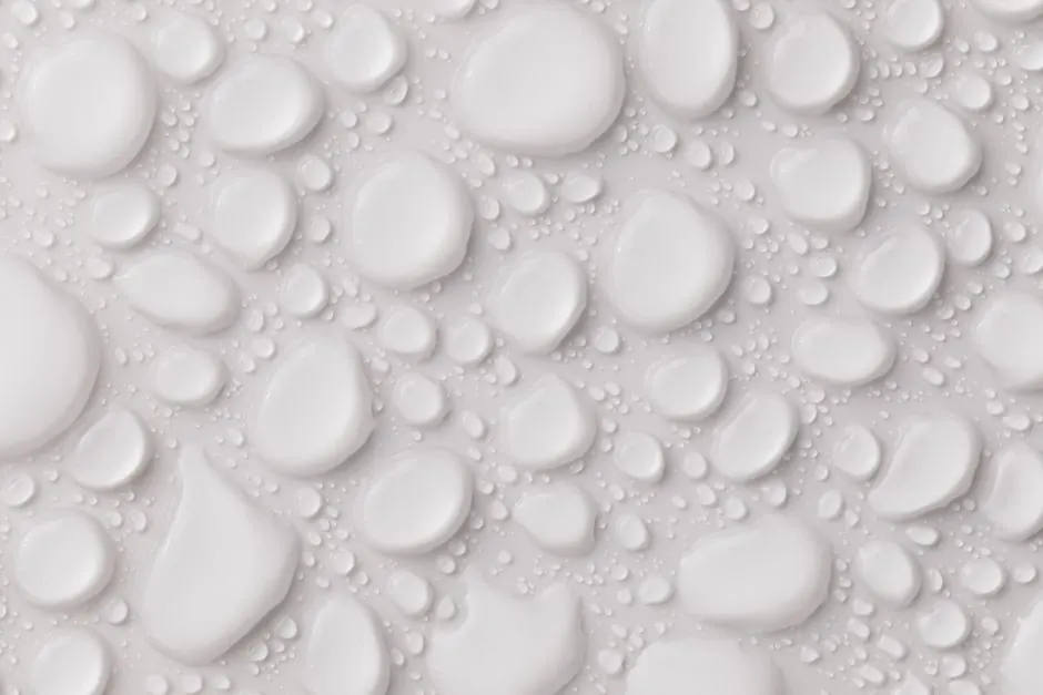 Closeup top view of white plain even surface with many abstract still glassy liquid drops of different shapes and sizes